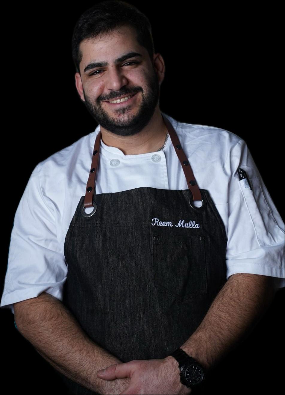 Chef Reem Mulla smiling in his white chef coat and dark apron